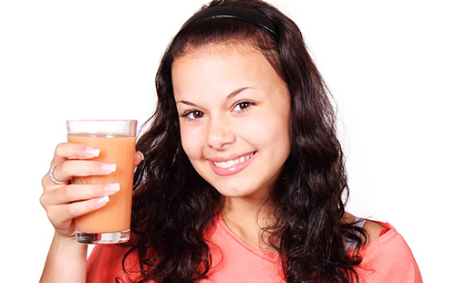 Девушка с лучезарной улыбкой держит в руке стакан морковного сока